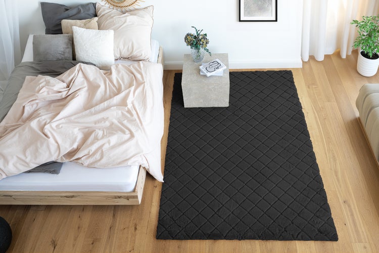 Ein rechteckiger Teppich mit Rautenmuster liegt neben einem Holzbett in einem hellen und modernen Schlafzimmer mit Holzboden.