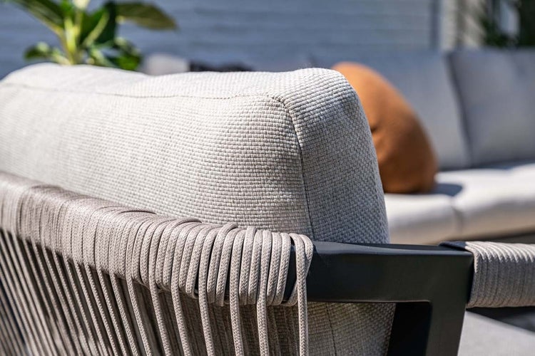 Detailansicht eines Gartensofas mit hellgrauem Textilbezug und dekorativer Seilbespannung an der Armlehne.