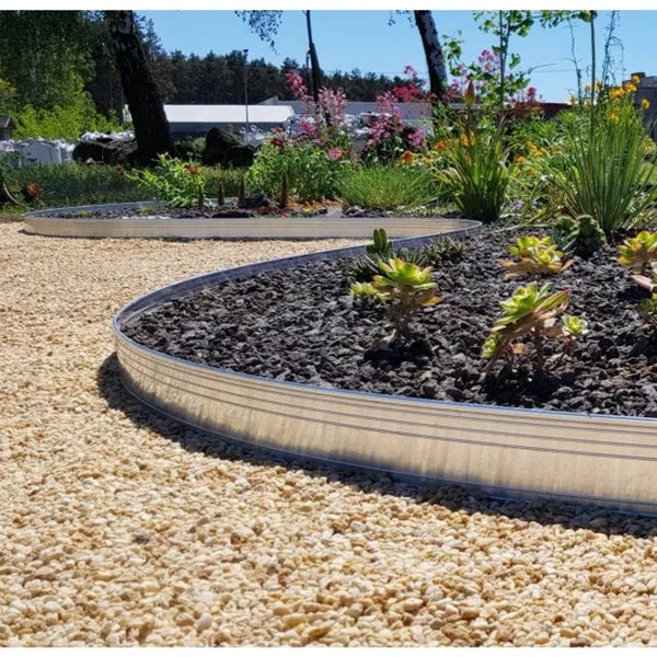 Flexible Rasenkante aus Metall in einem Garten zur Trennung von hellem Kies, dunklem Gestein und Pflanzen.