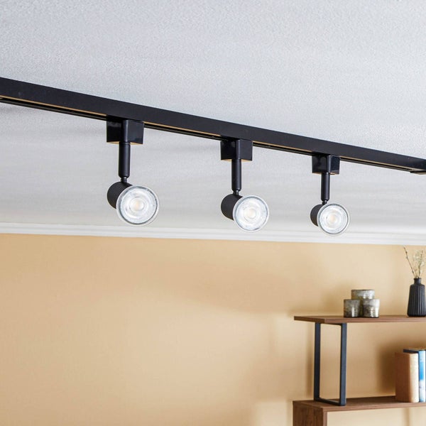 Schwarzes Schienensystem mit drei verstellbaren Strahlern an einer weißen Decke in einem hellen Wohnraum.