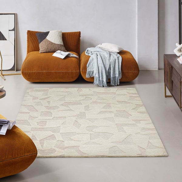 Moderner Wohnraum mit einem hellbeigen Teppich mit geometrischem Muster, zwei orangefarbenen Cord-Sesseln und einem Sideboard aus Holz.