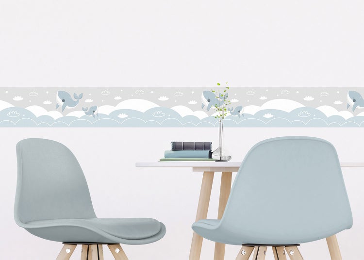Tapetenbordüre mit Walen, Wolken und Sternen in einem hellen Kinderzimmer mit Tisch und blauen Stühlen.