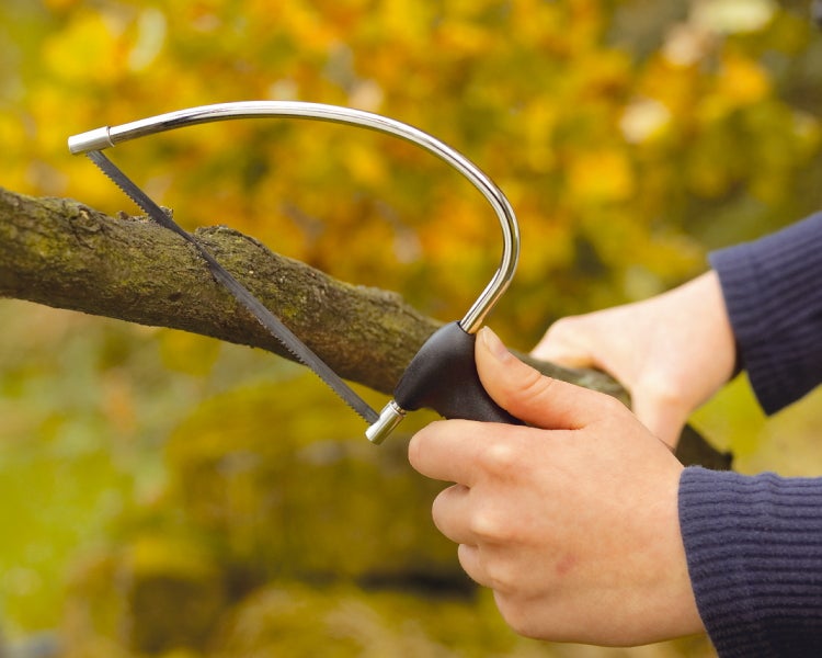Eine Person sägt einen Ast mit einer Handsäge mit gebogenem Metallrahmen im Garten.