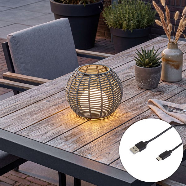 Dekorative LED Tischleuchte im Korbdesign fuer den Aussenbereich mit aufladbarem Akku und USB Ladekabel auf einem Holztisch.