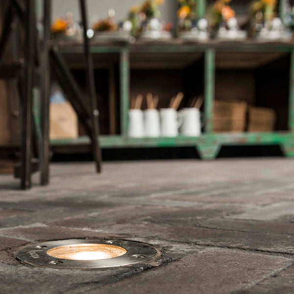Bodeneinbaustrahler aus Edelstahl in einem Steinboden mit warmweißem Licht.