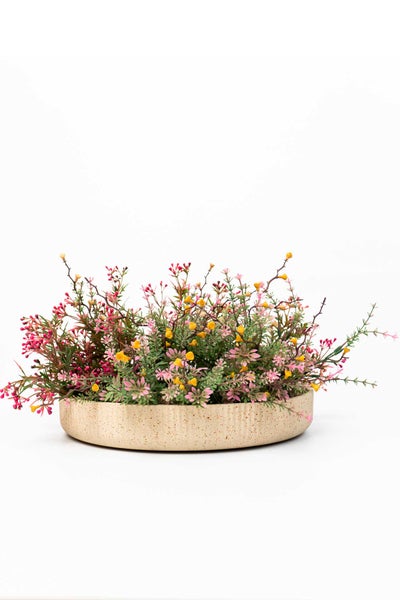 Kunstpflanze in flacher, gesprenkelter Keramikschale mit kleinen rosa und gelben Blüten.