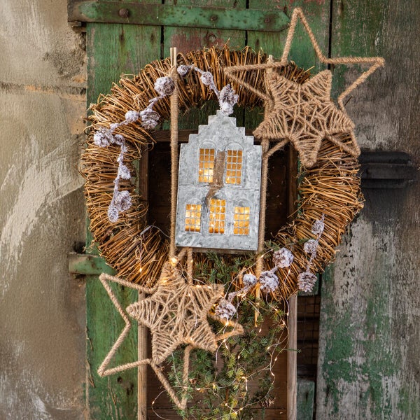Weihnachtskranz aus Zweigen mit integriertem Metallhaus, zwei Sternen aus Juteseil, Tannenzweigen und einer LED Lichterkette als Türschmuck.
