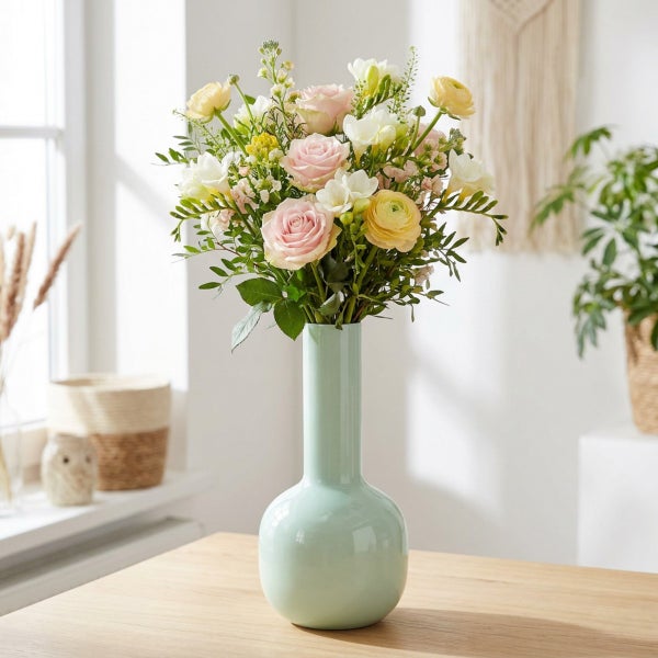 Blumenstrauß aus Rosen und Ranunkeln in einer bauchigen Vase auf einem Holztisch.