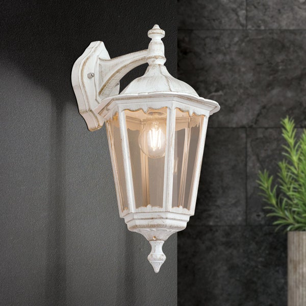 Klassische Außenwandleuchte im Laternen-Stil mit antikem Finish und klaren Glasscheiben, beleuchtet und an einer Wand montiert.