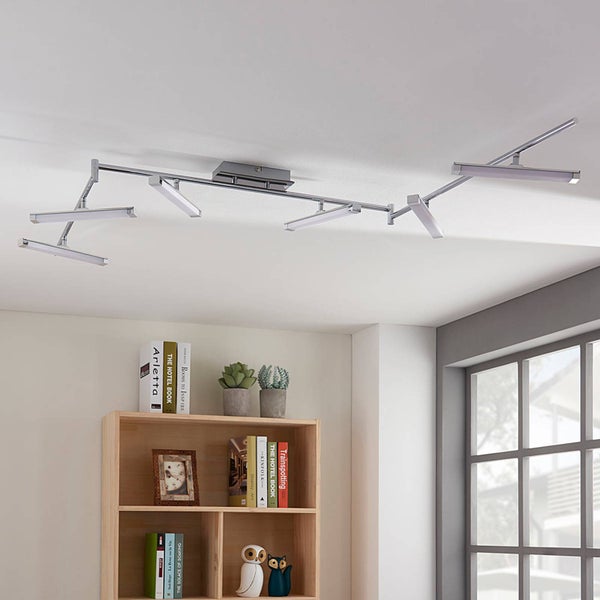 Moderne mehrflammige LED-Deckenleuchte mit verstellbaren Metallarmen in einem hellen Wohnzimmer über einem Bücherregal.