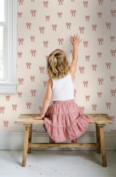 Kindertapete mit Schleifenmuster in einem hellen Zimmer mit Kind auf einer rustikalen Holzbank.