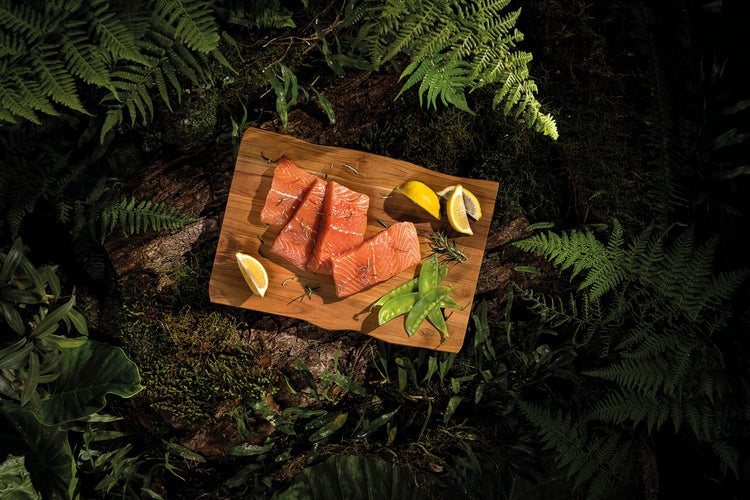 Holzbrett mit Lachsfilet, Zitrone und Erbsen in einer natürlichen Waldumgebung.