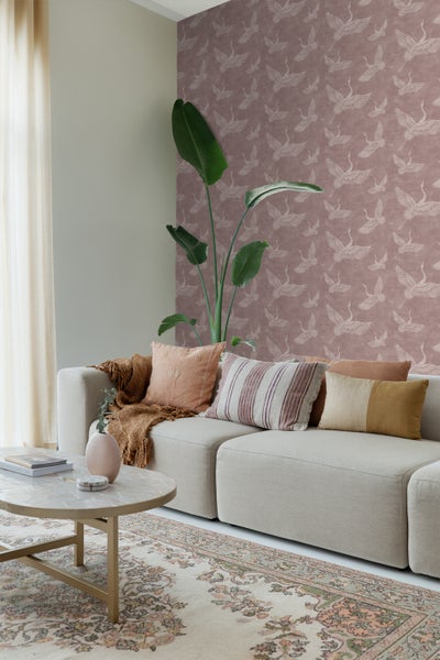 Wohnzimmer mit Sofa, Kissen, Teppich und gemusterter Tapete mit Kranichmotiven