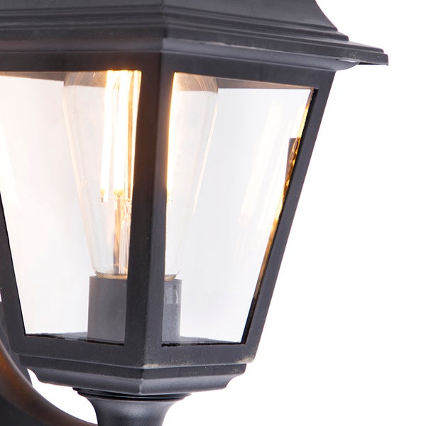 Nahaufnahme einer schwarzen Außenwandleuchte im Laternen-Stil mit klarem Glas und eingeschaltetem LED-Filament-Leuchtmittel.