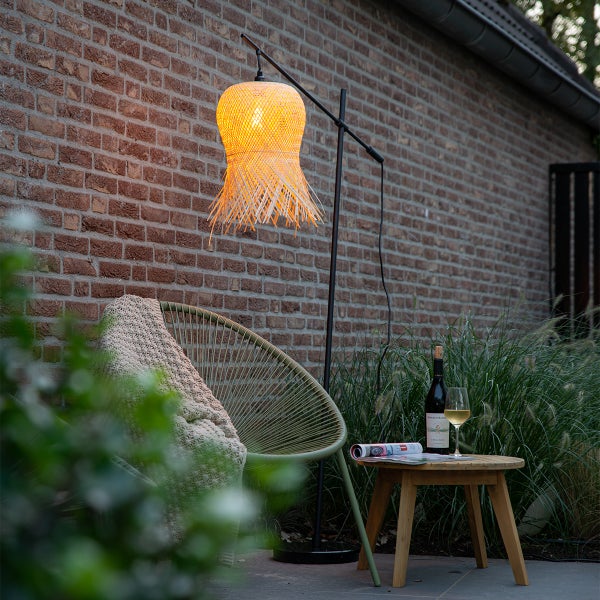 Moderne Terrasse mit beleuchteter Stehleuchte mit Geflecht-Schirm, Lounge-Sessel mit Decke und Holztisch mit Wein vor einer Backsteinwand.