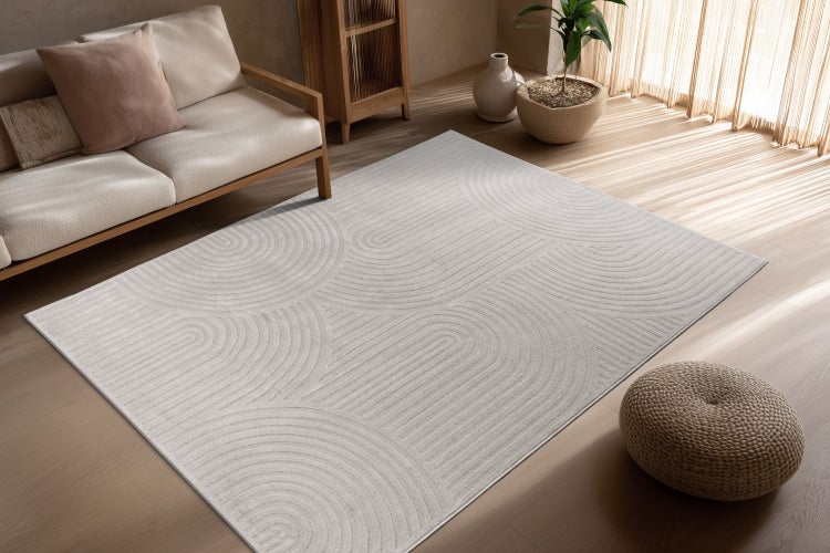 Rechteckiger Teppich mit modernem, geometrischem Linienmuster in einem hellen Wohnzimmer mit Sofa und Holzmöbeln.