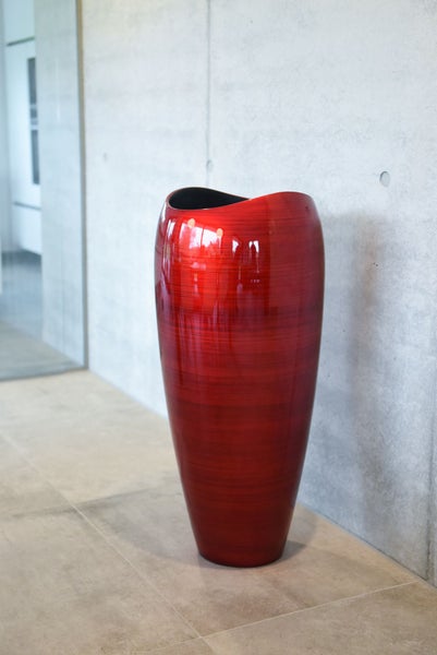 Hohe rote Bodenvase mit glänzender strukturierter Oberfläche in einem hellen Raum vor einer Wand in Betonoptik.