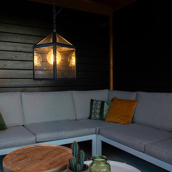 Hängeleuchte im Laternendesign mit Glas und Metallrahmen über einem Eck-Loungesofa mit grauen Polstern und Holzcouchtisch im Außenbereich.