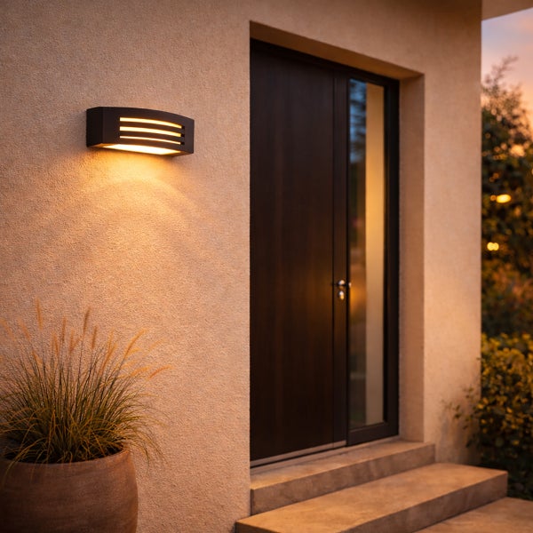 Moderne Außenwandleuchte mit warmem Lichtschein an einer Hausfassade neben einer dunklen Eingangstür aus Holz.