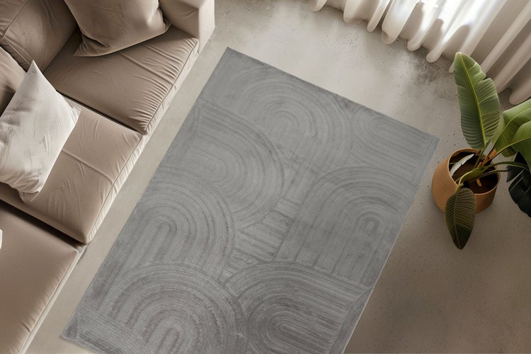 Rechteckiger Teppich mit abstraktem geometrischem Bogenmuster in einem modernen Wohnzimmer mit Sofa und Zimmerpflanze.