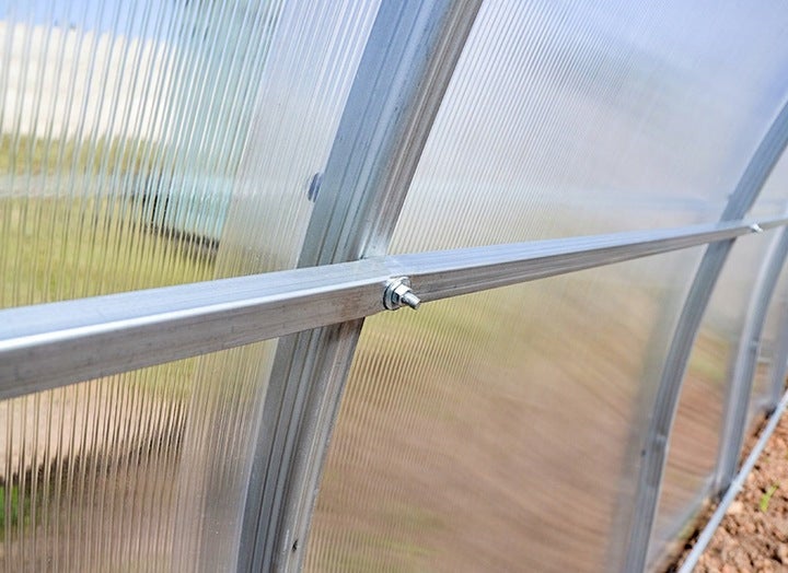 Nahaufnahme einer Aluminium-Profilverbindung mit Schraube und Mutter an einer Gewächshauswand aus Polycarbonat-Stegplatten.