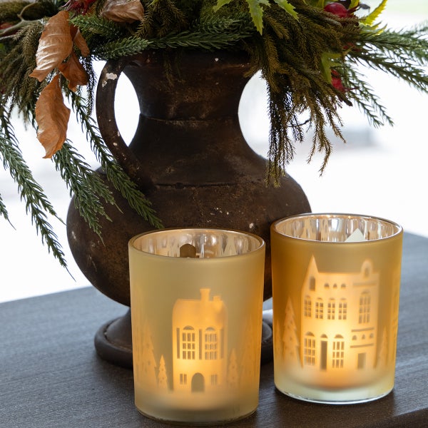 Zwei Teelichthalter aus Glas mit Hausmuster und eine Vase mit Dekoration.