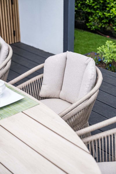 Moderner Essbereich im Freien auf einer Terrasse mit einem Seilgeflechtstuhl mit Polstern neben einem Holztisch.