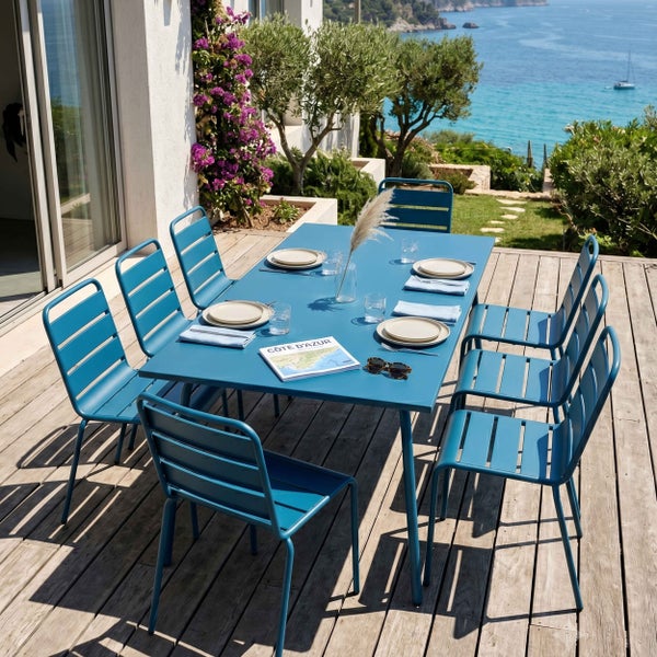 Gartenmöbel-Set aus blauem Metall mit rechteckigem Tisch und acht Stühlen auf einer Holzterrasse mit Meerblick im mediterranen Stil.