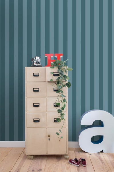 Szene mit gestreifter Tapete, Kommode mit Schubladen, Dekoration und Schuhen auf Holzboden.