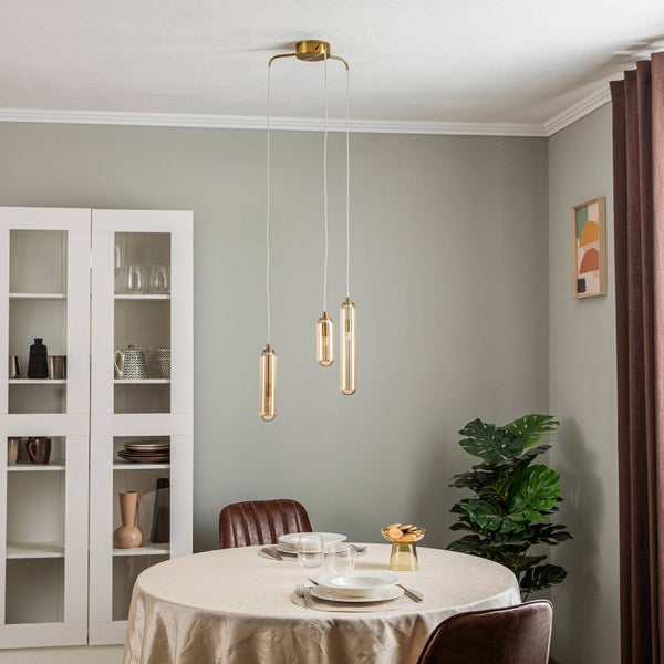 Moderne dreiflammige Pendelleuchte mit zylindrischen Schirmen aus bernsteinfarbenem Glas über einem gedeckten Esstisch in einem hellen Esszimmer.