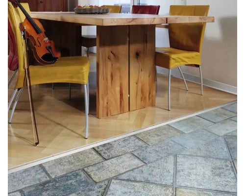 Übergangsprofil zwischen hellem Holzparkett und grauen Steinfliesen in einem hellen Esszimmer mit Holztisch und gelben Stühlen.