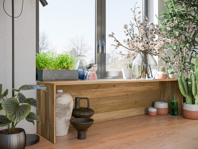 Helle, organisierte Raumszene mit einer niedrigen Holzbank unter einem Fenster, dekoriert mit verschiedenen Zimmerpflanzen in Glas- und Keramikgefäßen.