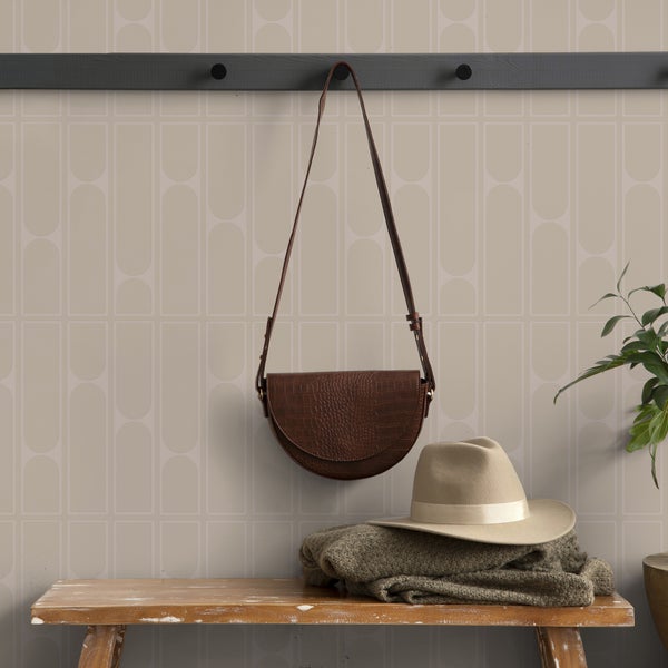 Szene mit brauner Handtasche, Hut und Pullover auf einer Holzbank vor einer Wand mit geometrischer Tapete.