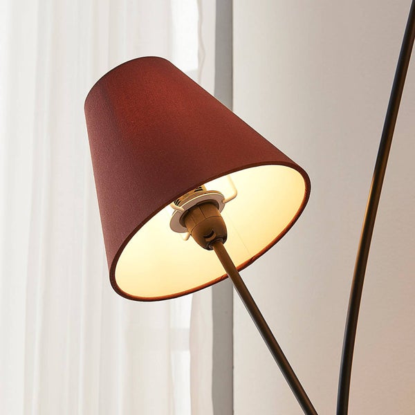 Detailansicht einer Lampe mit konischem, dunkelrotem Textilschirm und beleuchtetem Innenraum an einem Metallgestell.