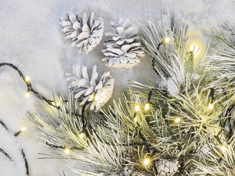 Weihnachtliche Tannenzweige mit Kunstschnee, Tannenzapfen und einer Lichterkette mit warmweißen Lichtpunkten als stimmungsvolle Dekoration.