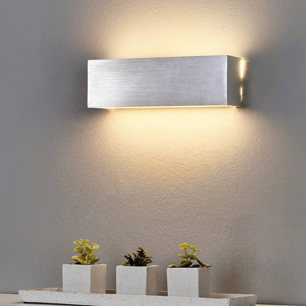 Moderne, rechteckige Wandleuchte aus gebürstetem Metall mit Licht nach oben und unten an einer Wand über kleinen Pflanzen in quadratischen Töpfen.