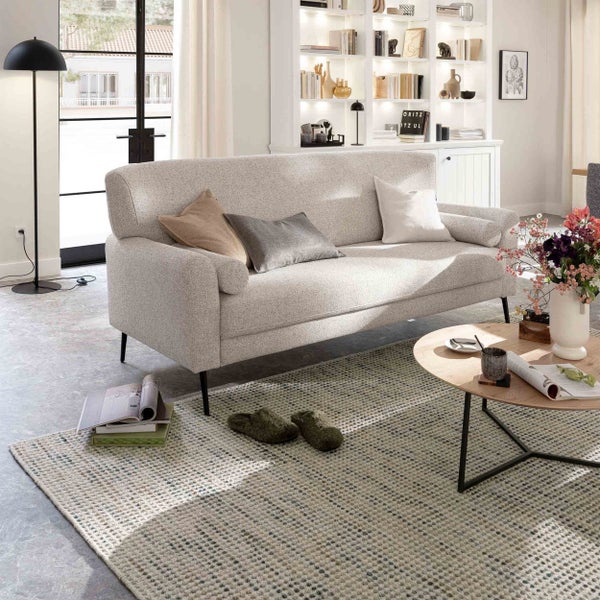 Modernes, helles Wohnzimmer mit einem Drei-Sitzer-Sofa aus strukturiertem Stoff, einem runden Couchtisch aus Holz und einem gemusterten Teppich.