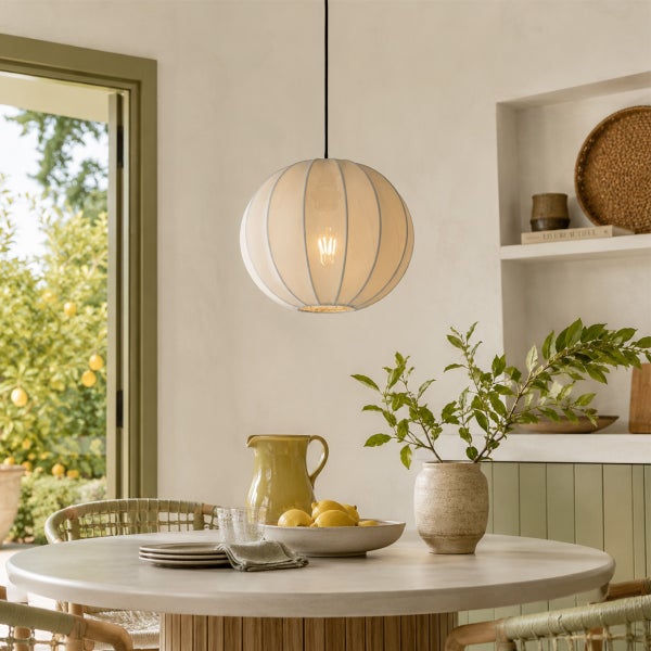 Helle Kugel Pendelleuchte mit Stoffschirm über einem runden Esstisch in einem hellen, mediterran eingerichteten Esszimmer mit Blick in den Garten.