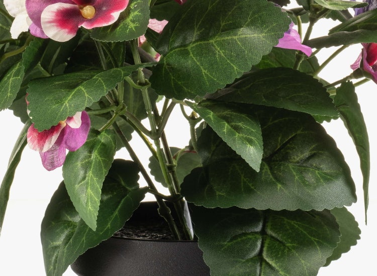 Künstliche Saintpaulia mit grünen Blättern und violett-rosa Blüten in einem schwarzen Topf.