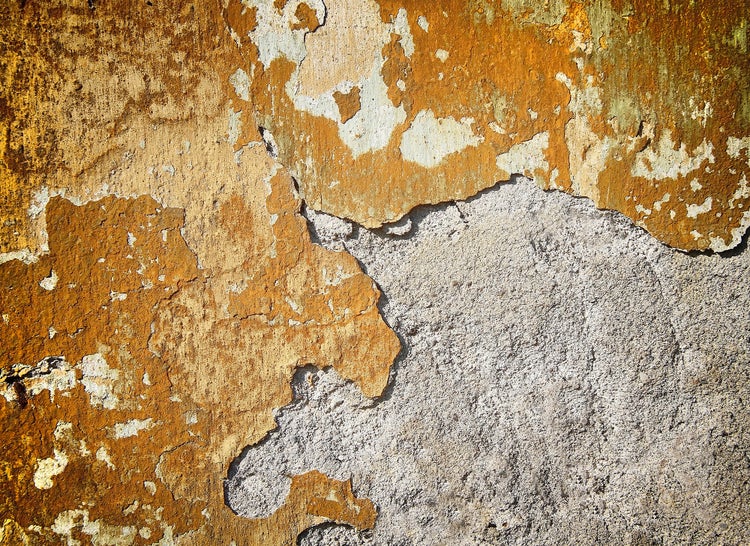 Detailaufnahme einer Wand mit abblätternder Farbe und grobem, freiliegendem Putz.