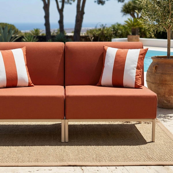 Terracottafarbenes Gartensofa mit gestreiften Kissen auf einer Terrasse neben einem Pool und einem gewebten Teppich.