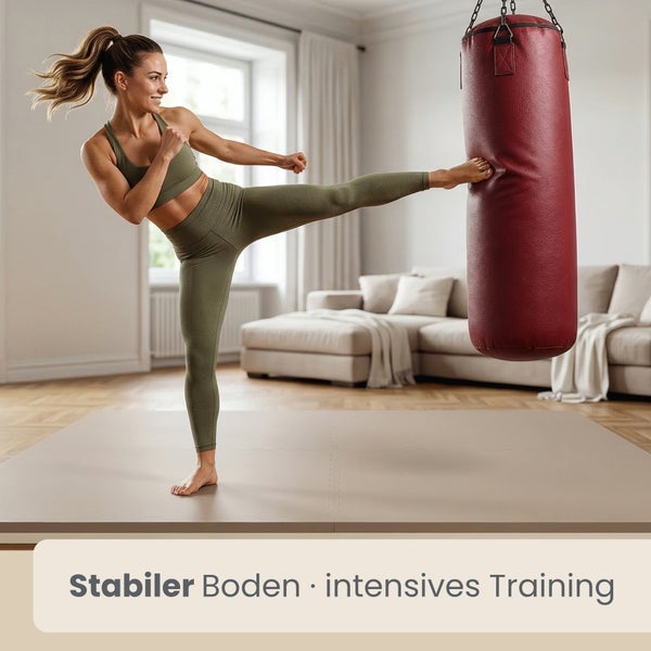 Frau beim Kampfsporttraining auf einer stabilen Bodenschutzmatte vor einem roten Boxsack in einem hellen Wohnzimmer.