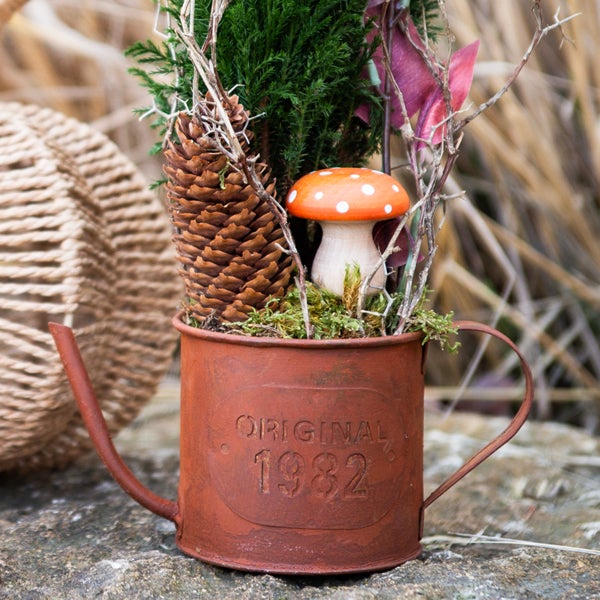 Dekorative Gießkanne mit Pflanzen, Zapfen und Pilz als Tischdekoration