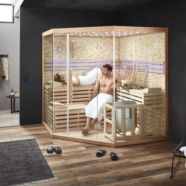 Ein Mann entspannt in einer modernen Sauna mit Holzbank, Steinwandverkleidung, LED Beleuchtung und Saunaeimer.