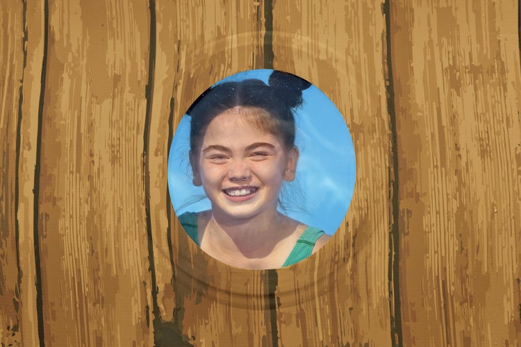 Rundes Bullauge in einer Wand mit Holzoptik, durch das ein lächelndes Mädchen schaut.