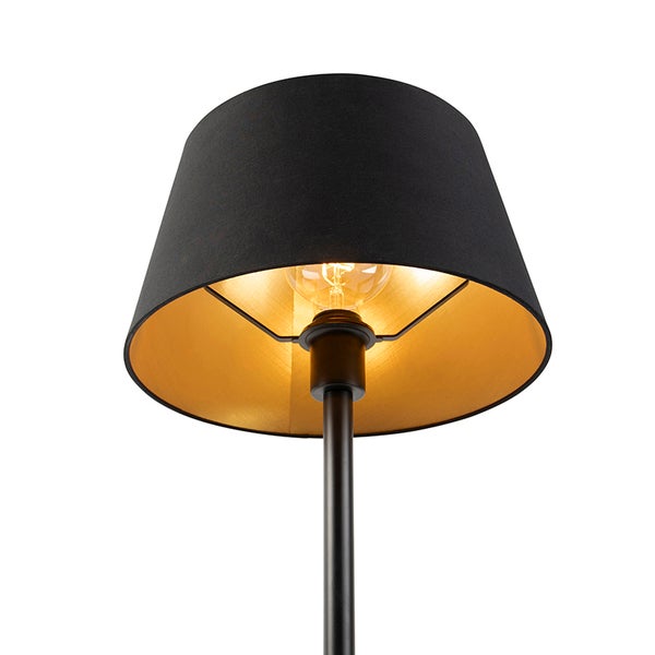 Lampenschirm aus schwarzem Stoff mit goldener Innenseite, schwarzer Metallständer, eingeschaltetes Leuchtmittel.