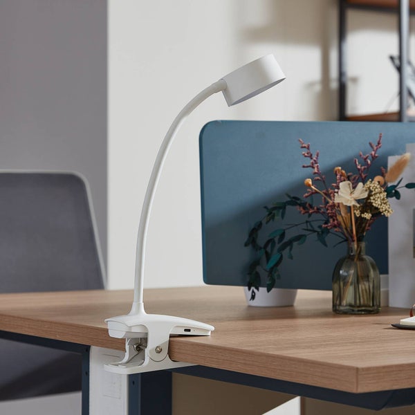 Weiße LED-Klemmleuchte mit flexiblem Hals an einem Schreibtisch aus Holz in einem hellen, organisierten Büro.