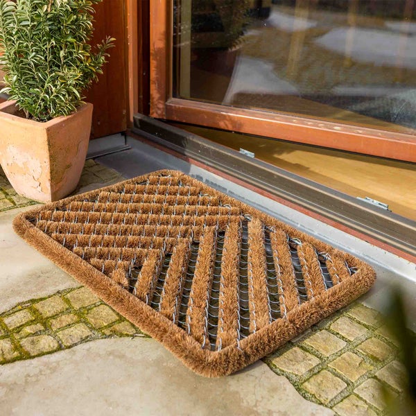 Fußmatte aus Kokosfasern vor einer Haustür mit Pflanze im Topf