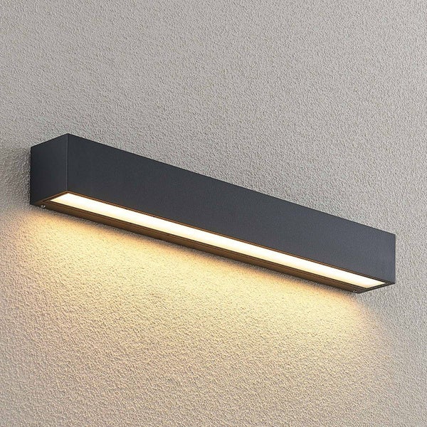 Moderne, längliche LED-Wandleuchte aus Metall in Anthrazit mit warmweißem Lichtschein nach unten auf einer strukturierten Wand.