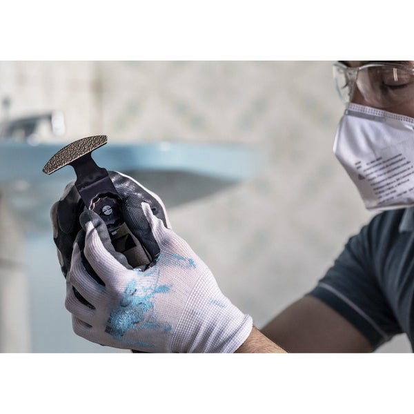 Mann mit Schutzbrille und Atemschutzmaske hält ein Multifunktionswerkzeug Schleifblatt.